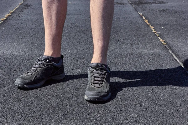 The legs of a man in black sneakers. Black and gray asphalt background. The concept of running and walking. Legs of young man in black sneakers.