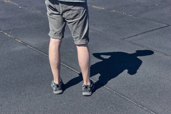 The legs of a man in short shorts and black sneakers. Black and gray asphalt background. The concept of running and walking. Legs of young man in black sneakers.