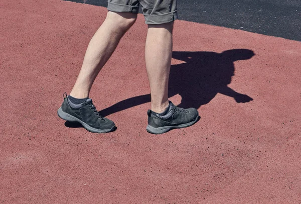 The legs of a man in short shorts and black sneakers. Red and brownasphalt background. The concept of running and walking. Legs of young man in black sneakers.