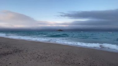 Mavi saatte deniz, ufukta küçük bir ada.