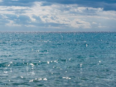 Mavi deniz ufku sabah güneşinin ışınlarında parıldıyor. Gökyüzünde yumuşak bulutlar var.