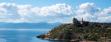 Sardinya 'daki Calamosca Dağı boyunca uzanan deniz ve beyaz deniz feneri kulesi, güneşli bir günde mavi gökyüzü ve tüylü beyaz bulutlarla kaplı. Web pankartı