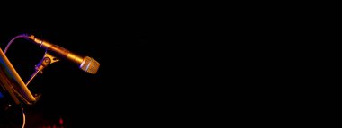 Bir tarafta turuncu renkli ışıklar, siyah arkaplan web sayfası fotokopi alanı ile aydınlatılmış bir konser sırasında mikrofon var.