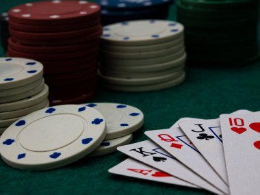 Yeşil keçeli masa arka planında poker fişleri yığılı Royal straight floş poker kartları