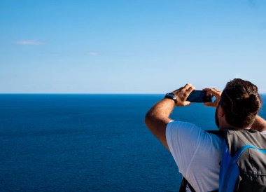 Kafkasyalı genç adam deniz kenarında akıllı telefonuyla fotoğraf çekiyor.