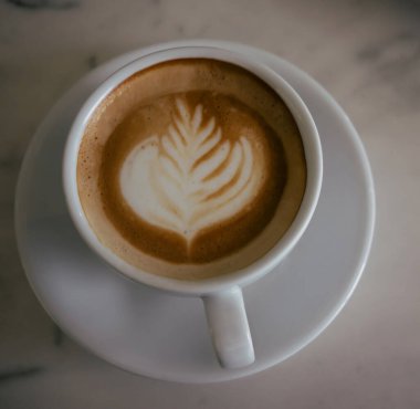 Süt köpüğüyle betimlenmiş bir buğday bitkisinin latte sanatı, mermer masada bir tabak kapuçino.