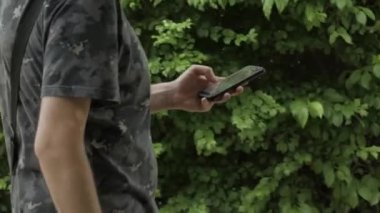 side shot of a young man walking at the park using a mobile phone