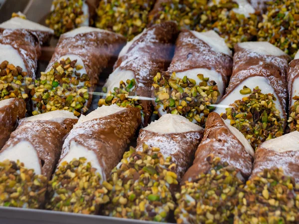 assortment of various Sicilian cannoli with chopped pistachios and filled with ricotta cheese for sale in a pastry shop