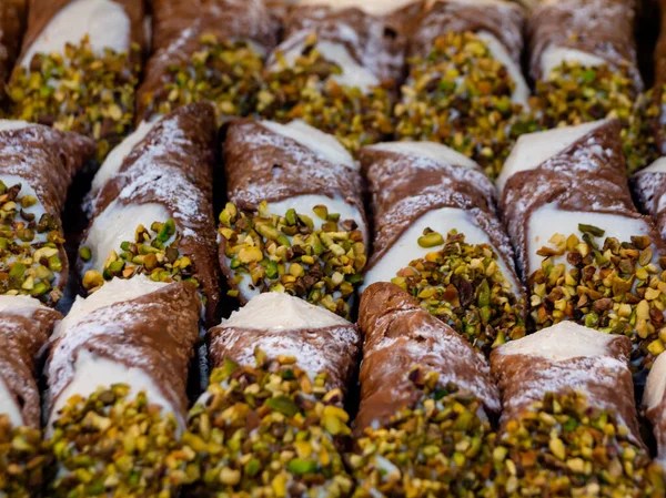 assortment of various Sicilian cannoli with chopped pistachios and filled with ricotta cheese for sale in a pastry shop