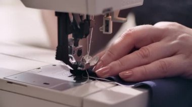 Kadınların elleri dikiş makinesine mavi bir kumaş dikiyor.