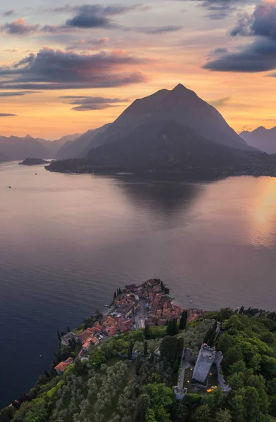 Vezio Kalesi 'nin dikey panoramik manzarası, Varenna köyü ve yaz günbatımında arka planda dağlar. Como Gölü 'nde İHA atışı. Varenna, İtalya