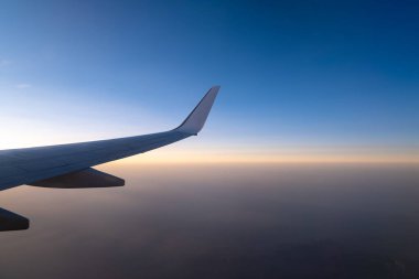 Uçuyor ve seyahat ediyor, günbatımında uçağın penceresinden bakıyor..