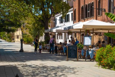 VENICE, İtalya - 27 Ağustos 2021: Venedik sokaklarındaki tipik bir İtalyan restoranında yemek yiyen ailelerin görüntüsü.