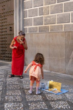 GRANADA, SPAIN - SEPTEMBER 25, 2021: View of beautiful little girl giving a coin to street artist in Granada.
