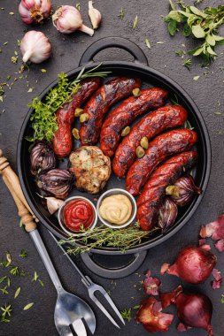 Üzerine hardal ve ketçap eklenmiş ızgara sosis koyu arkaplanda dökme demir bir tabakta servis edilir.