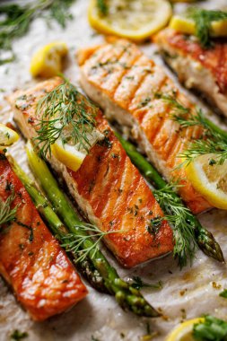 Fırınlanmış somon filetosu ve aromatik otlar ve limonlu yeşil kuşkonmaz. İçindeki kısma odaklan, yakın plan.
