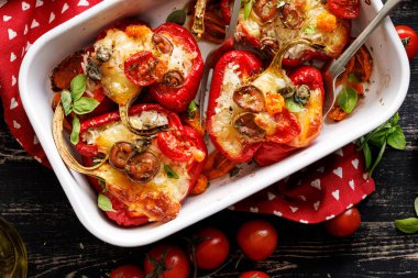 Pirinç, sebze ve mozzarella peyniri ile doldurulmuş kırmızı dolma biberler. Koyu ahşap bir masada, pişirme kabında otlarla tatlandırılmış. Yakın görüş.