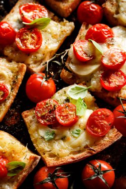 Siyah arka planda taze fesleğenle tatlandırılmış mozzarella peyniri ve kiraz domatesli baget tostları.