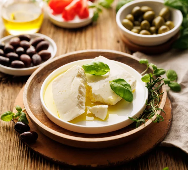 Feta cheese with the addition of olive oil and fresh basil leaves on a ceramic plate, close up view. Traditional Greek product