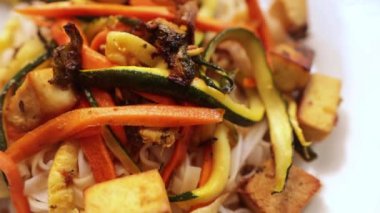 Sebzeli tofu tarifi, havuç, kabak, kırmızı ve yeşil biber ve beyaz tabakta Asya eriştesi.