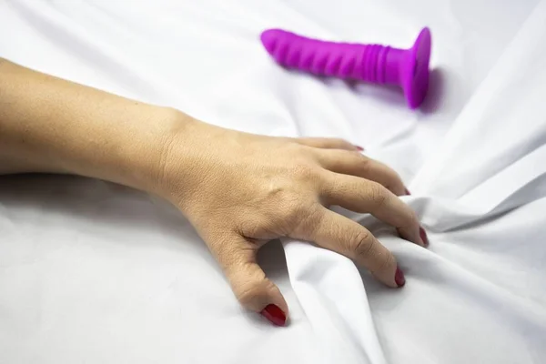 Concept of orgasm and sexuality, a girl's arm experiences sexual pleasure, she grabs the white sheets next to a pink dildo