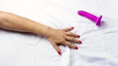 Concept of orgasm and sexuality, a girl's arm experiences sexual pleasure, she grabs the white sheets next to a pink dildo