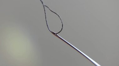 Threading a needle with sewing thread, sewing concept, selective focus on the buttonhole with the thread, unfocused background