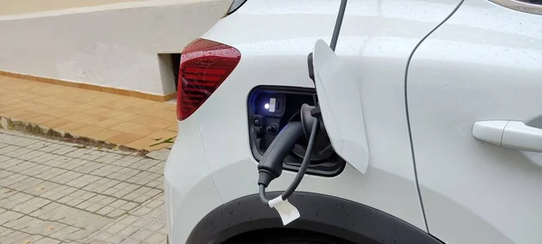 A white, electric car is charged on public roads, a concept of energy saving, availability of renewable energy to the user