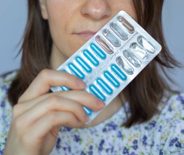 Genç bir kız ya da kadın elinde mavi bir vitamin ve mineral kompleksi tutuyor. Yüze ve haplara odaklan.