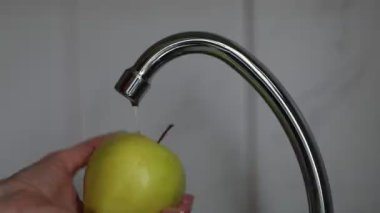 Sarı elmayı musluk suyunun altında yıkıyorum. Bir kadının eli bir elmayı yıkar.