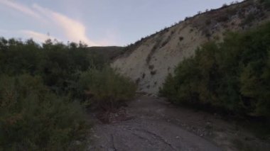 Granada 'nın güneyinde kurumuş bir nehrin videosu var. Taşlar ve kum var. Ağaçlar ve çalılar var.