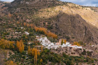  Granada 'nın güneyinde küçük bir kasaba, kasaba dağlık bir bölgede, kasabanın bir kilisesi ve evleri beyaza boyanmış, ağaçlar var.