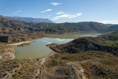 mountainous landscape in southern Spain, there are trees and bushes, there is a water reservoir, the sky is clear