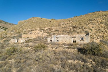 ruined farmhouse in southern Spain, it is a mountainous area, there are trees and shrubs, the sky is clear