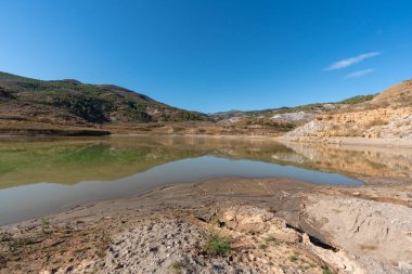 mountainous landscape in southern Spain, there are trees and bushes, there is a water reservoir, the sky is clear