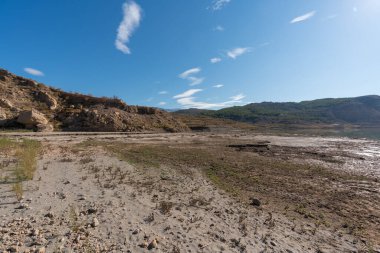 mountainous landscape in southern Spain, there are trees and bushes, there is a water reservoir, the sky is clear