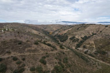 İspanya 'nın güneyindeki dağlık arazi, ağaçlar ve çalılar var, toprak yollar var, gökyüzü bulutlu.