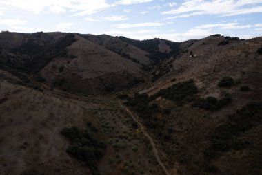 Granada 'nın güneyindeki dağda bir vadi, ağaçlar ve çalılar var, gökyüzünde bulutlar var.