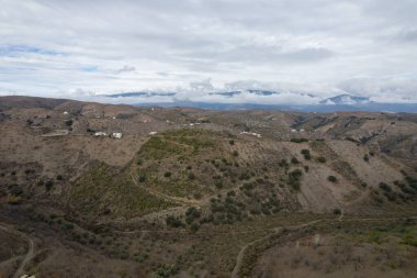İspanya 'nın güneyindeki dağlık arazi, ağaçlar ve çalılar var, toprak yollar var, gökyüzü bulutlu.