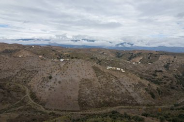 İspanya 'nın güneyindeki dağlık arazi, ağaçlar ve çalılar var, toprak yollar var, gökyüzü bulutlu.