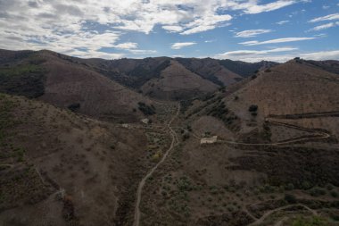 İspanya 'nın güneyindeki dağlık arazi, ağaçlar ve çalılar var, toprak yollar var, gökyüzü bulutlu.
