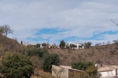 Granada 'nın güneyinde bir grup çiftlik evi, ağaçlar ve çalılar var, bir dağ bölgesi, gökyüzü bulutlu.