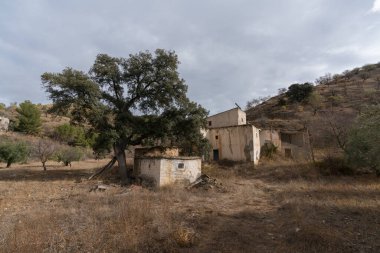 İspanya 'nın güneyindeki dağlık arazi, ağaçlar ve çalılar var, bir kır evi var, gökyüzü bulutlu.