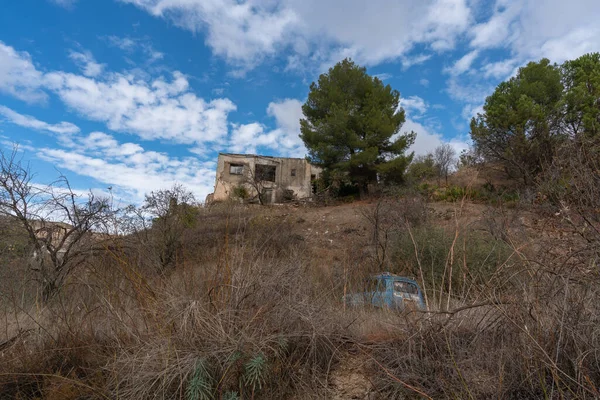İspanya 'nın güneyindeki dağlık bir bölgede eski bir kır evi, ağaçlar ve çalılar var, eski bir araba var, gökyüzü bulutlu.