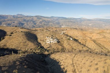 Granada 'nın güneyindeki dağlık alanda, dağın yamacında küçük bir kasaba var, badem ekinleri var, gökyüzünde bulutlar var.