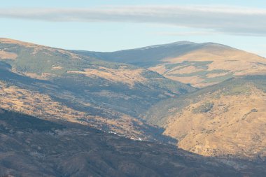 Güney İspanya 'daki Sierra Nevada dağları, dağlarda kar var, dağ yamacında ormanlar var, birkaç köy var, gökyüzü bulutlu.