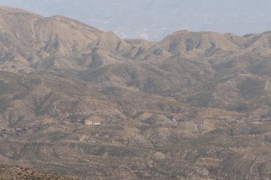 Almerya 'daki Tabernas Çölü' nün kurak manzarası (İspanya), dağlık bir manzaradır, birkaç ev, çalılıklar ve gökyüzü bulutludur.