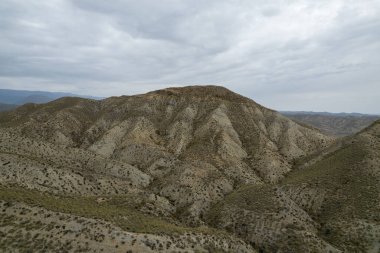 Almerya 'daki Tabernas Çölü' nün kurak manzarası (İspanya), dağlık bir manzara, çalılar var ve gökyüzü bulutlu.