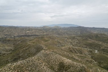 Almerya 'daki Tabernas Çölü' nün kurak manzarası (İspanya), dağlık bir manzara, çalılar var ve gökyüzü bulutlu.