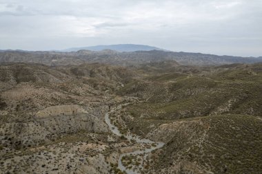 Almerya 'daki Tabernas Çölü' nün kurak manzarası (İspanya), dağlık bir manzara, çalılar var ve gökyüzü bulutlu.